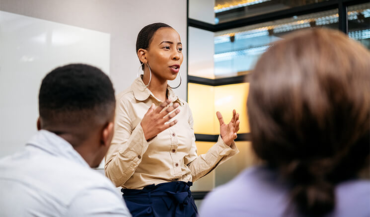 A woman standing in a meeting room and explaining to others 