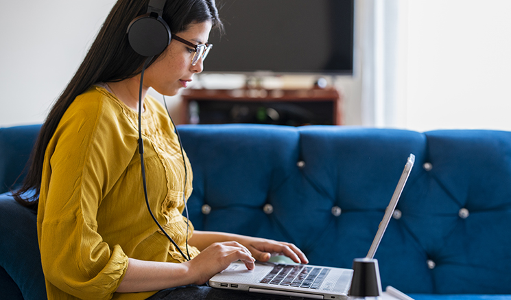 Mujer con una camisa amarilla usando auriculares mientras usa su computadora portátil