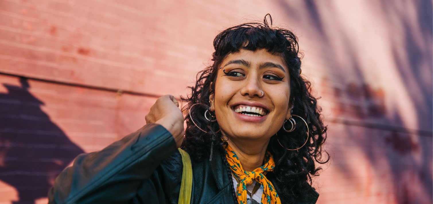 College-aged woman with nose ring and hoop earrings smiles while looking off to the left