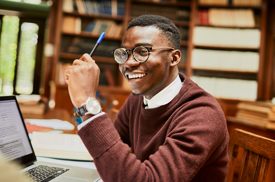 Young man with glasses and holding up a pen in a library
