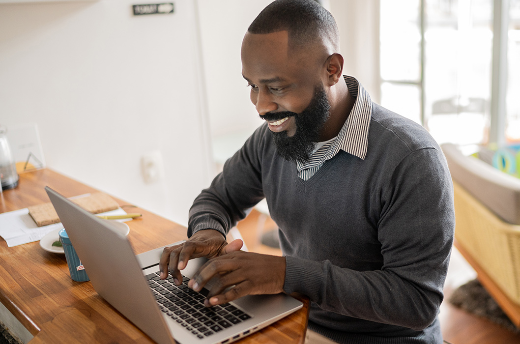 Bearded black man in a sweater and collared shirt using a laptop