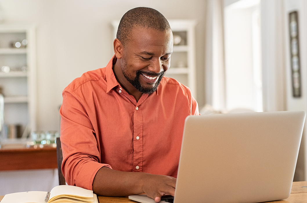 Bearded black man sitting and grinning while using his laptop at home