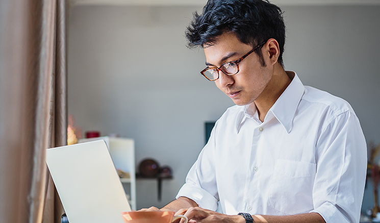 Jeune homme d’affaires asiatique travaillant avec un ordinateur portable assis dans un café