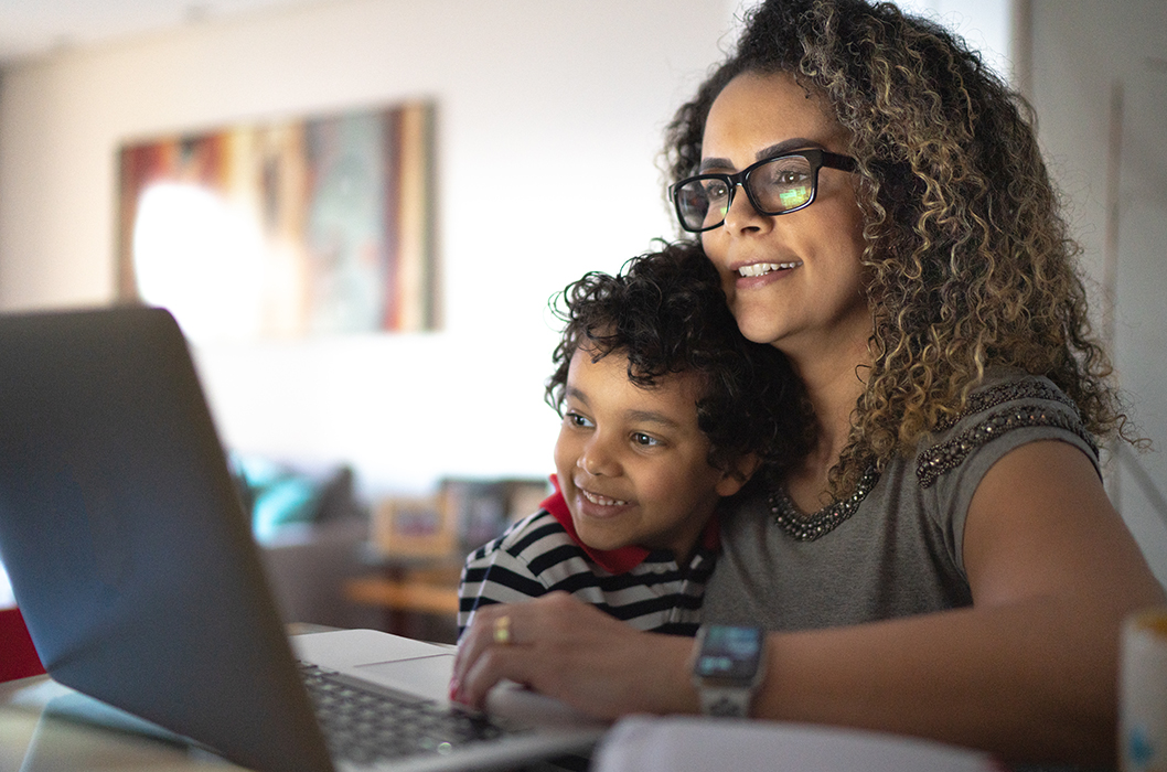 1255718526 Mature woman working at home, carrying young son